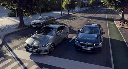 Drei BMW Limousinen stehen auf einer Straße in einer städtischen Umgebung.